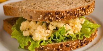 Homemade egg salad with leafy green lettuce between two slices of multi-grain bread.